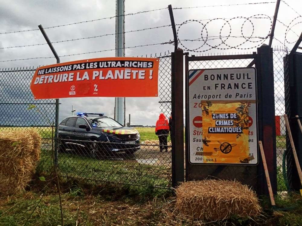 Fence of the airport cut out, with XR and Attac banners by the side