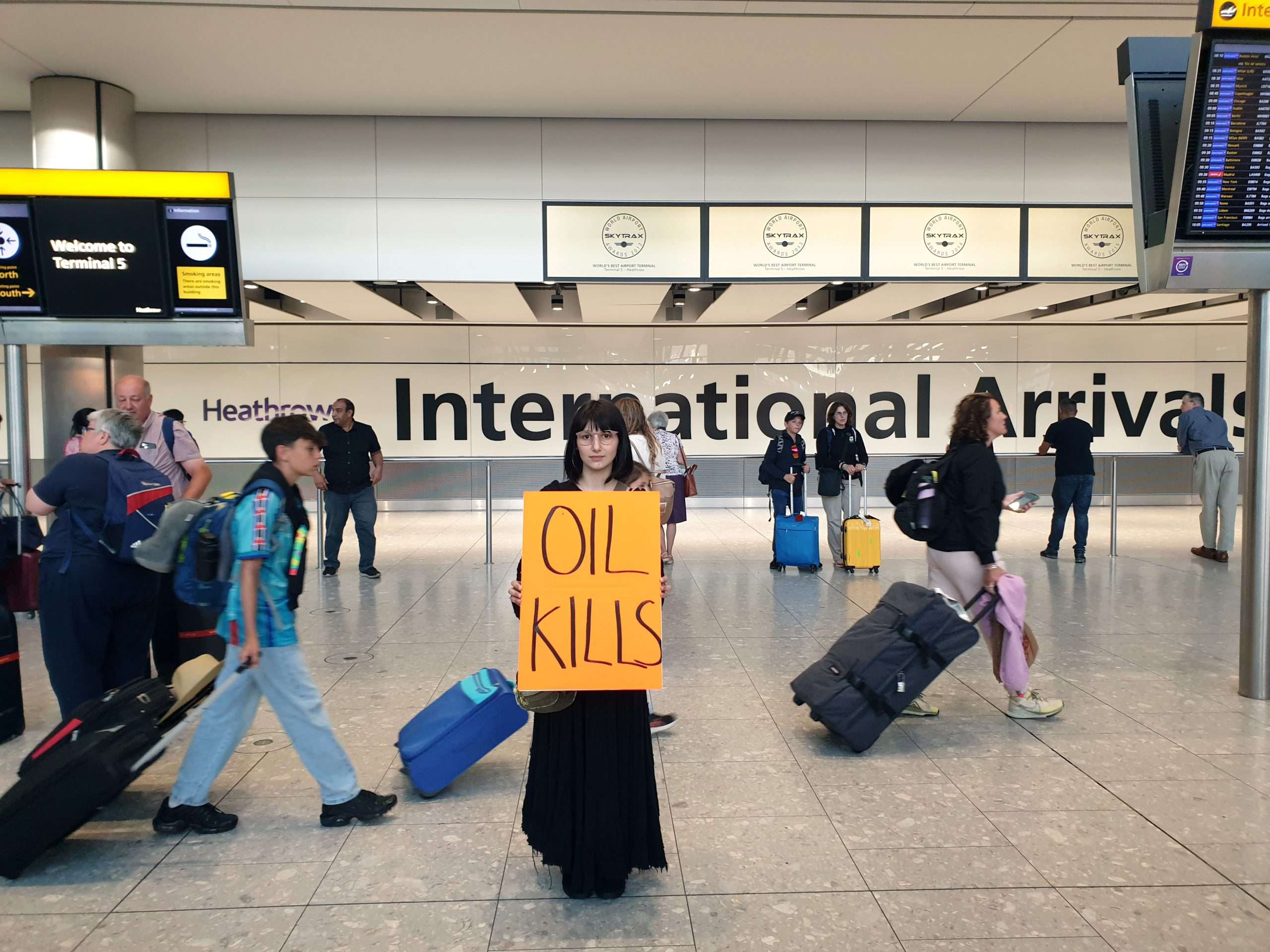IMAGE_JustStopOil_Heathrow1_27072024 Just Stop Oil supporter holding "Oil Kills" banner, at Heathrow Airport.